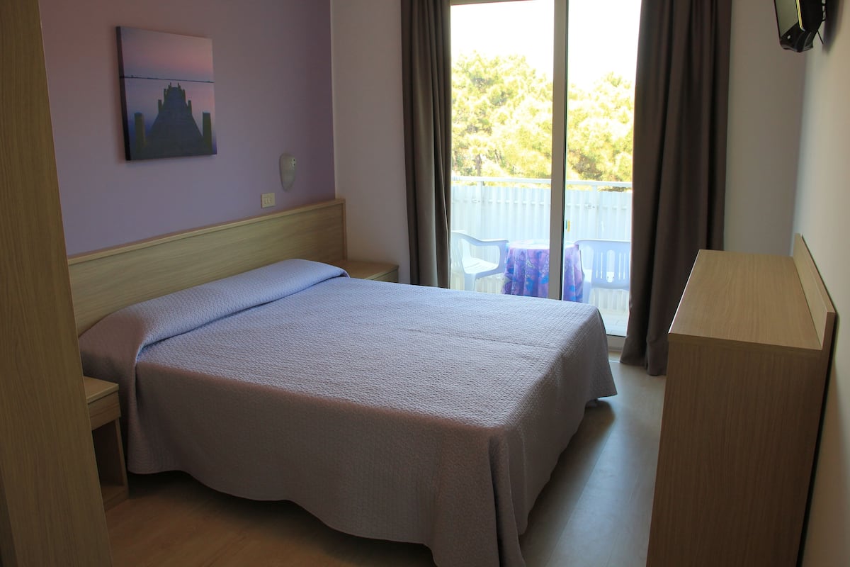 Une chambre à coucher comprenant un lit, une table de chevet, un bureau, une chaise et une fenêtre avec des rideaux.