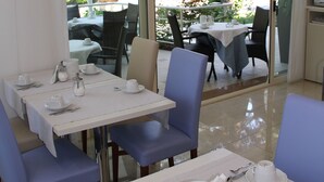 A dining area with tables and chairs, a view of the outdoors, and a glass door leading outside.
