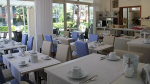 A dining area with tables set for breakfast, featuring white tablecloths, plates, cups, and cutlery.