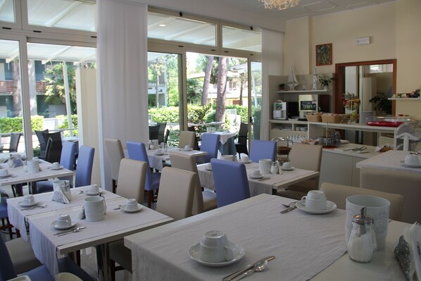 A dining area with tables set for breakfast, featuring white tablecloths, plates, cups, and cutlery.