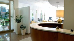 A reception area with a curved wooden desk, a lamp, and potted plants.