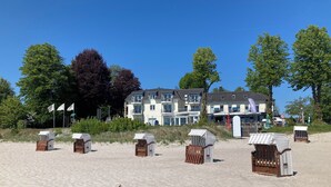 Un hotel frente a la playa con varios balcones, cabañas de playa y un cielo azul despejado.