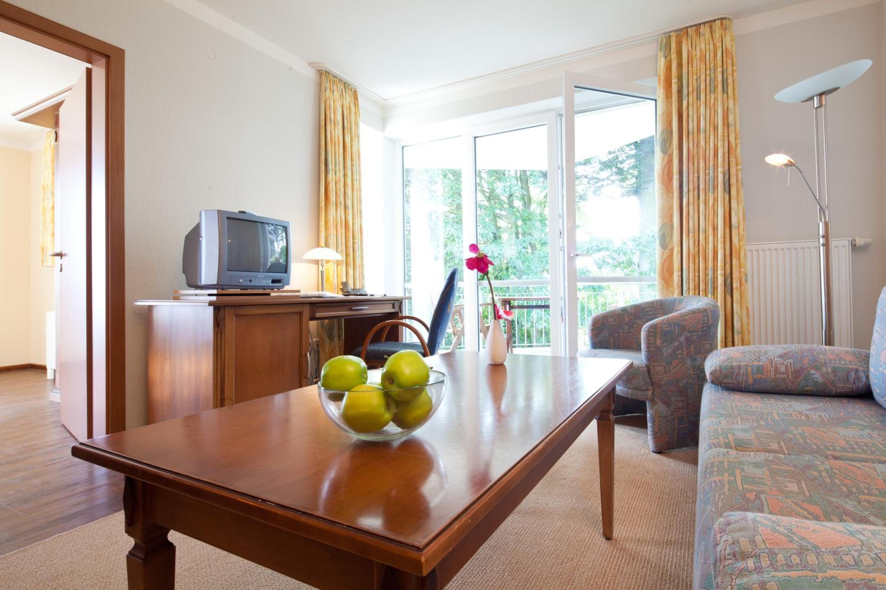 Una sala de estar con una mesa de madera, un televisor, un sofá y vistas al exterior a través de un ventanal.