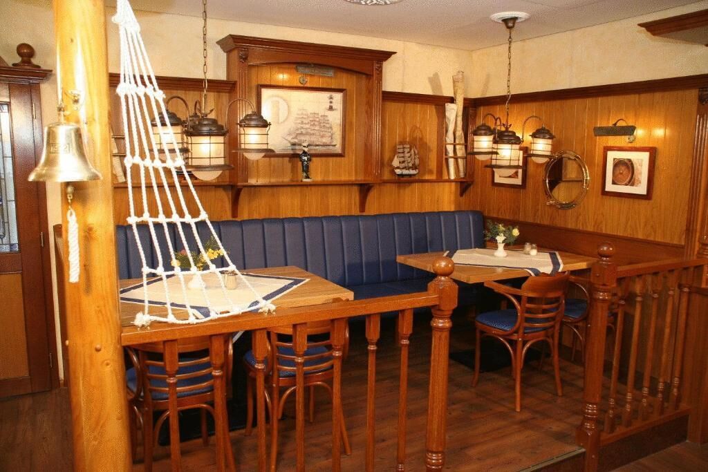Un interior de madera con una mesa, sillas, un banco acolchado azul y faroles en la pared.