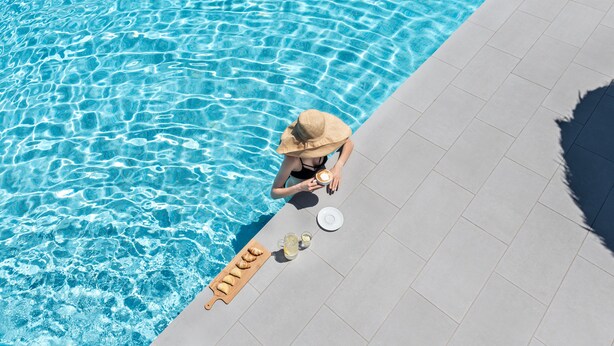 A poolside view with clear water, a sun lounger, and a beverage tray. - Rivari Hotel (Santorini)