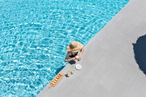 A poolside view with clear water, a sun lounger, and a beverage tray. - Rivari Hotel (Santorini)