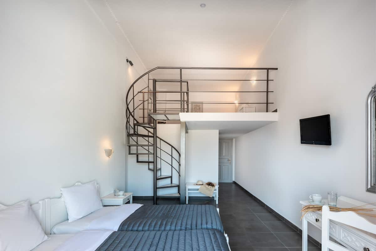 Una habitación de hotel moderna con cama, escritorio, silla, televisor y una escalera en espiral que conduce a un nivel superior.