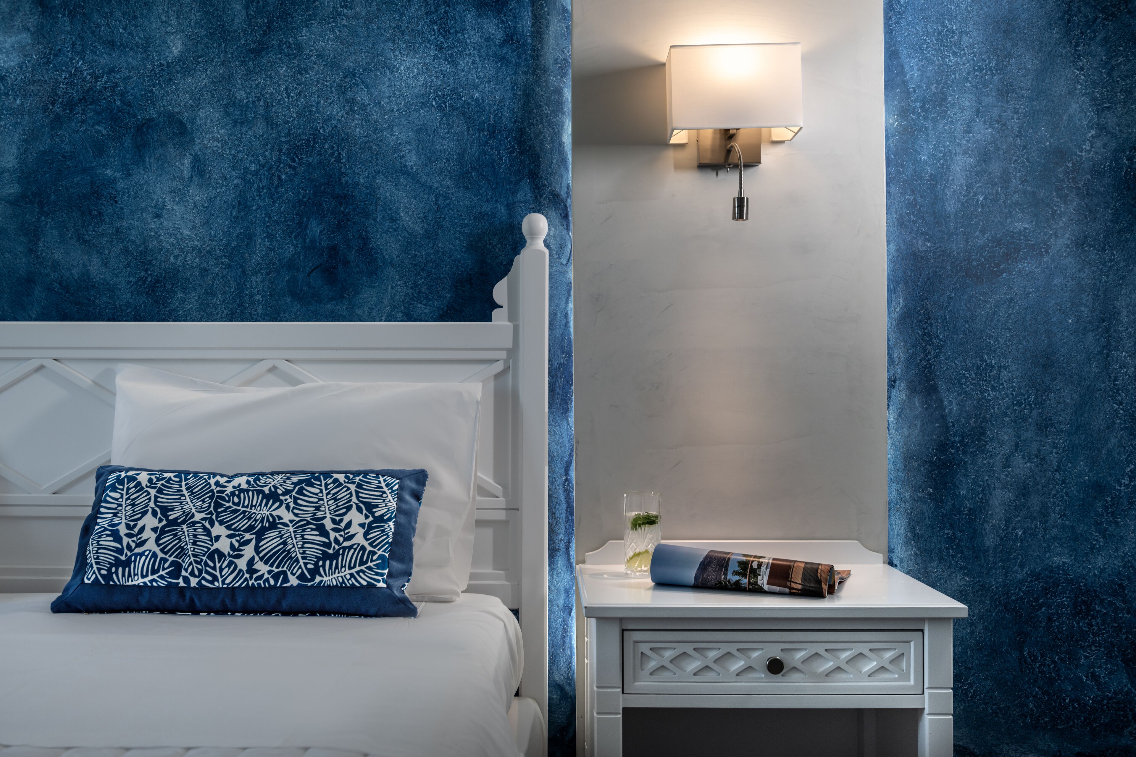 A bedroom with a bed, a nightstand, and a wall-mounted lamp.