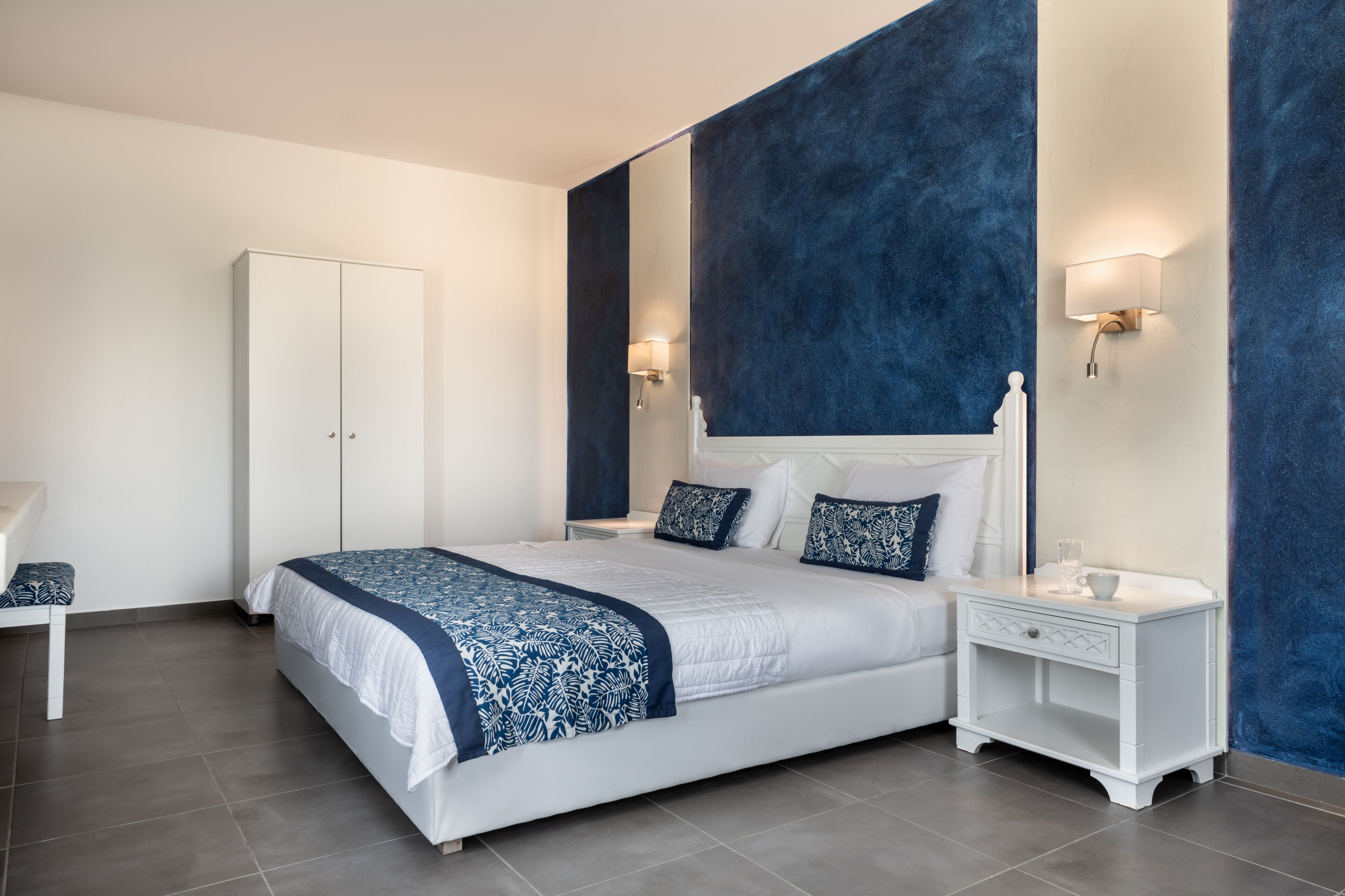 Un dormitorio moderno con una cama grande, mesitas de noche blancas y una pared azul de acento.
