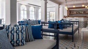 A spacious lounge area with a sofa set, patterned cushions, and a bar area with shelves of bottles. - Rivari Hotel (Santorini)