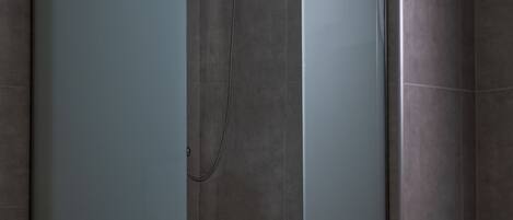 A modern shower enclosure with frosted glass doors, a handheld showerhead, and tiled walls.