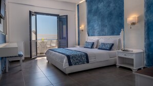 A modern bedroom with a large bed, a bedside table, a nightstand, and a view of the outdoors through an open door. - Rivari Hotel (Santorini)