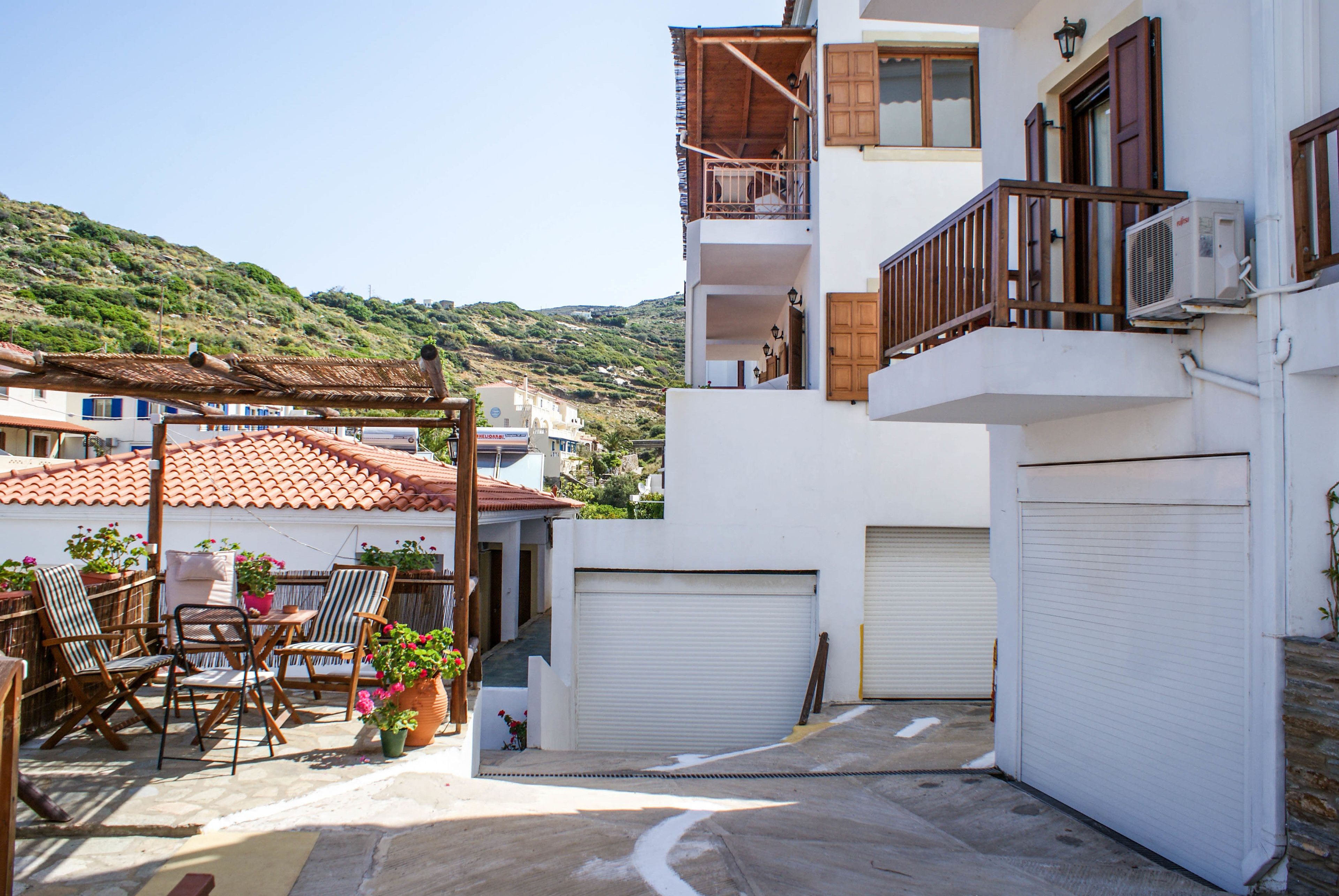 A residential building with a balcony, a garage, and a patio area with outdoor furniture and potted plants.