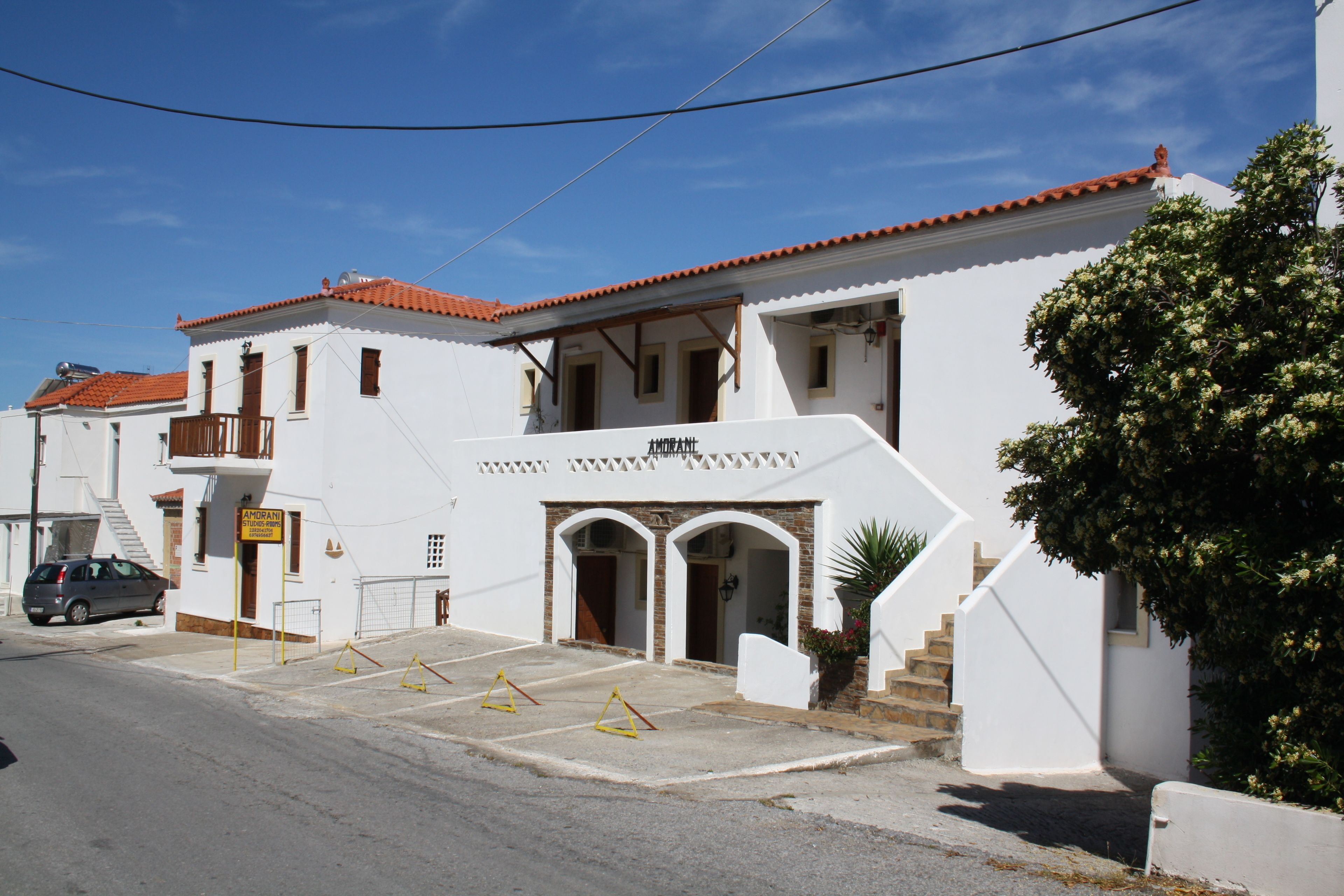 A white building with a red-tiled roof, a staircase leading to a balcony, and a sign indicating a business.