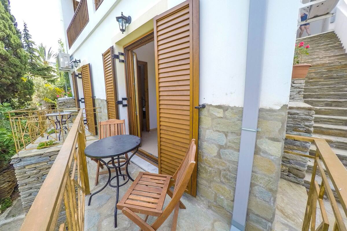 A balcony with a table and chairs, wooden shutters, and a stone wall.