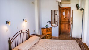 A bedroom with a bed, a nightstand with a telephone, a dresser, a mirror, and a door leading to another room. - Amorani Studios (Andros)