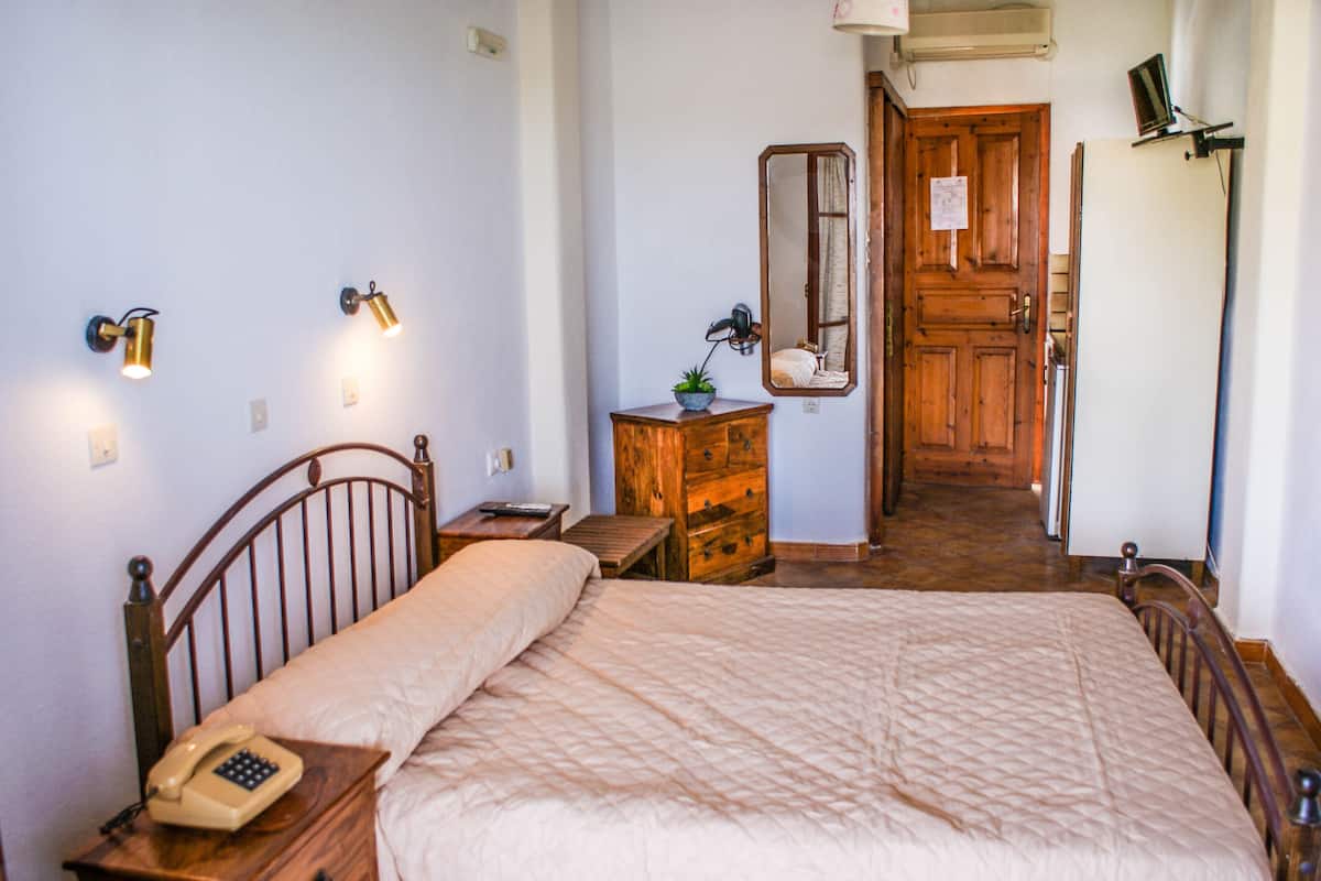 A bedroom with a bed, a nightstand with a telephone, a dresser, a mirror, and a door leading to another room.