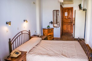 A bedroom with a bed, bedside table, lamp, dresser, mirror, and a door leading to another room. - Amorani Studios (Andros)