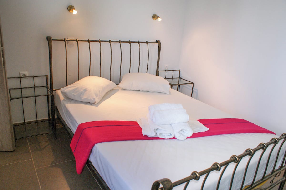 A neatly made bed with white linens, a red blanket, and folded towels.