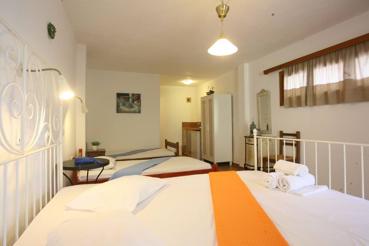 A hotel room with two single beds, a small table with a chair, a desk, a mirror, and a window with curtains.