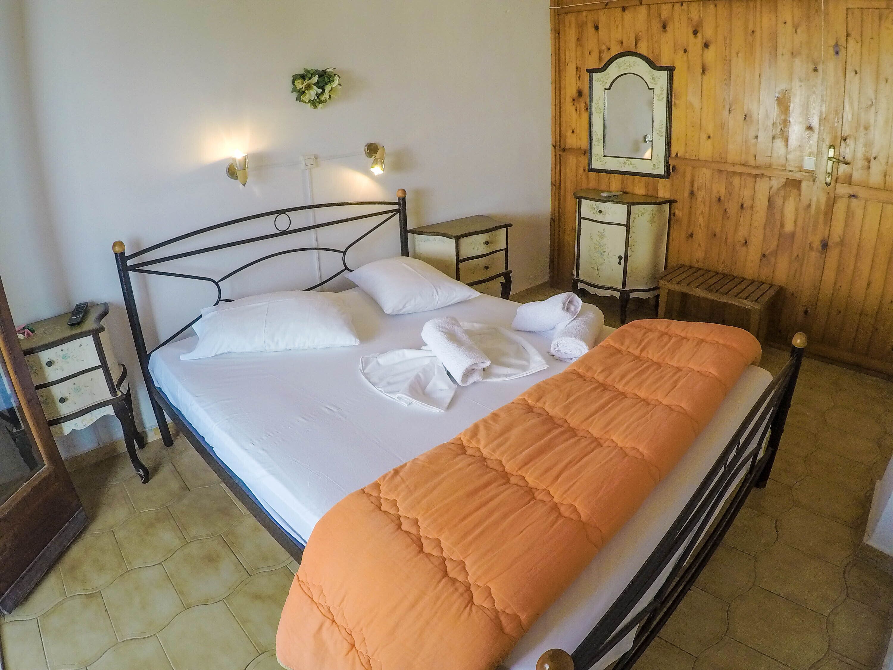Una cama bien hecha con ropa de cama blanca y naranja, un cabecero de madera y una mesita de noche con una lámpara.