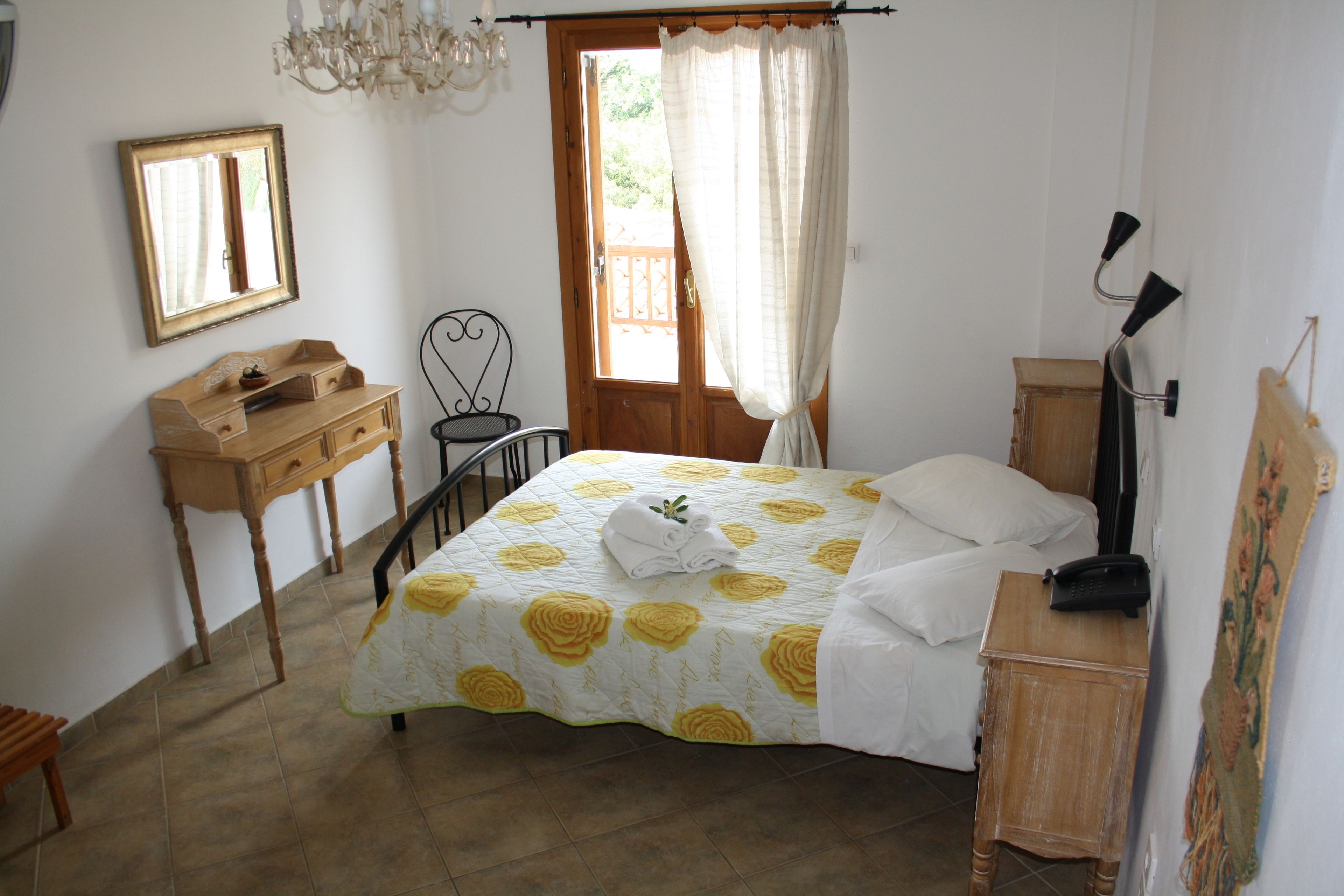 A bedroom with a bed, a desk, a chair, a mirror, and a door with curtains.