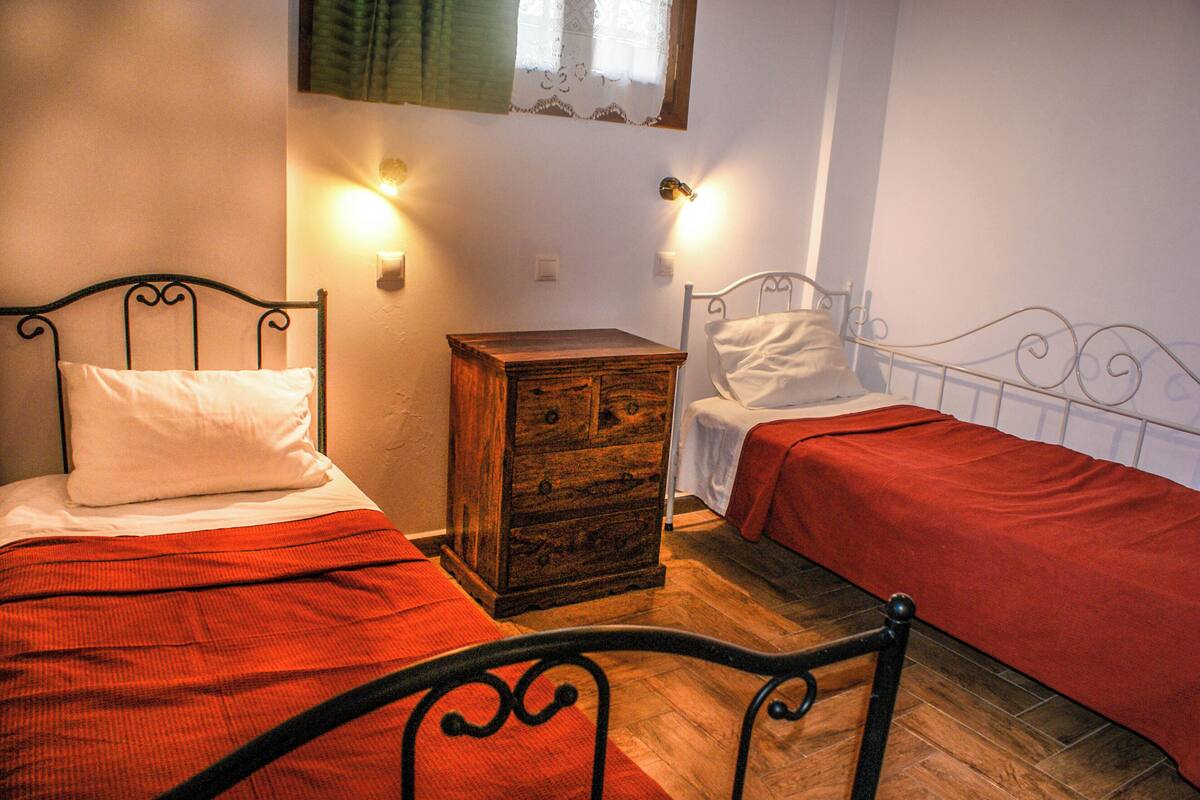 A room with two beds, each with a red bedspread and white pillows, a wooden dresser, and wall-mounted lights.
