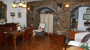 A dining area with a wooden table and chairs, a white armchair, and a brick wall with an arched doorway. - Amorani Studios (Andros)
