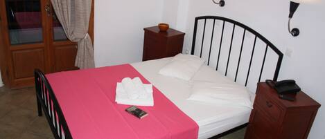 A bed with a pink bedspread, white pillows, and a wooden nightstand with a telephone.