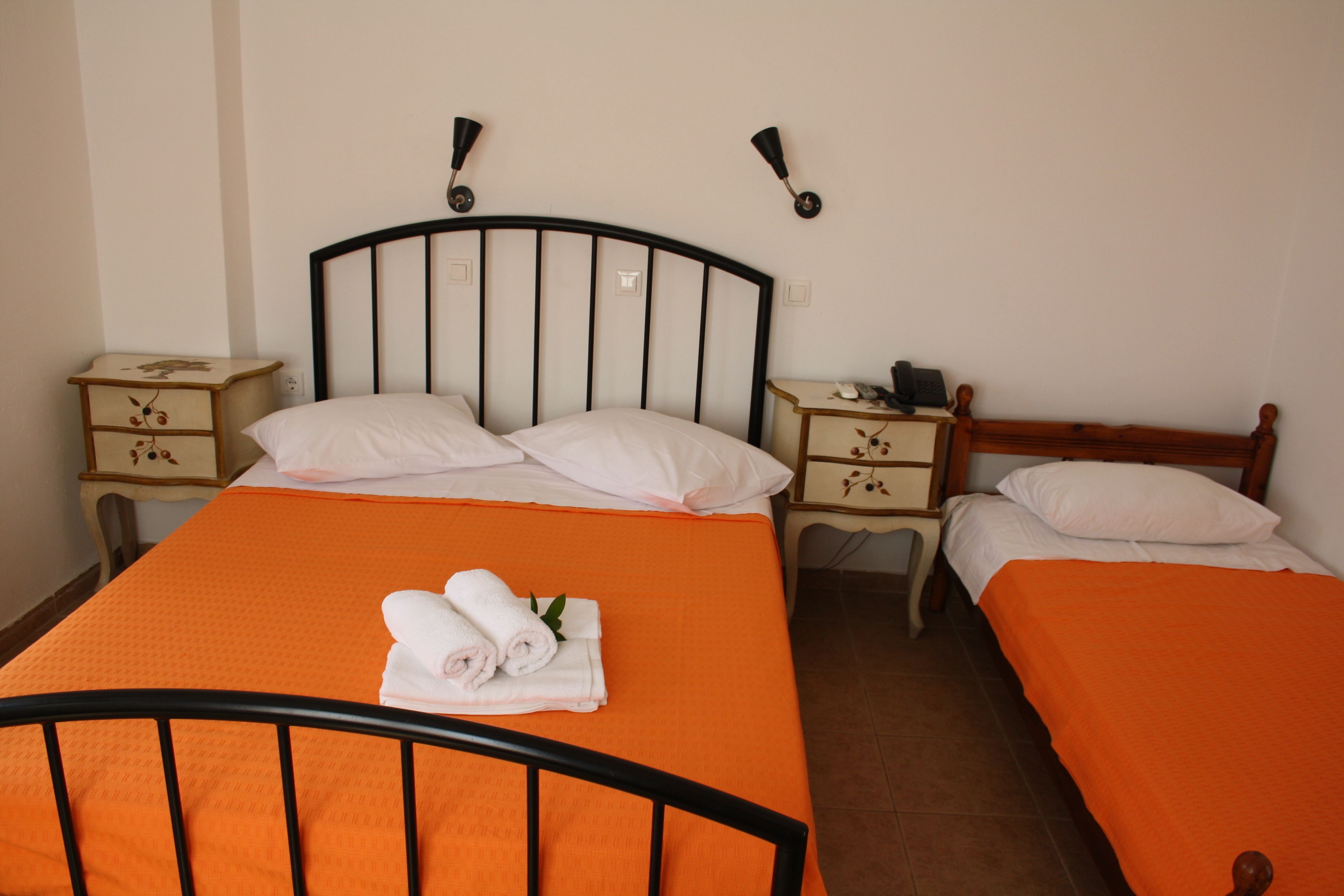 Una camera da letto con due letti, ognuno con una coperta arancione e cuscini bianchi. Sono presenti due comodini con lampade e una testiera in legno.