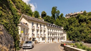 Een hotel met meerdere balkons, een stenen muur en een geparkeerde auto.