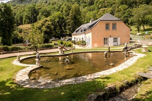 Una casa con un estanque, rodeada de follaje y un sendero de piedra.