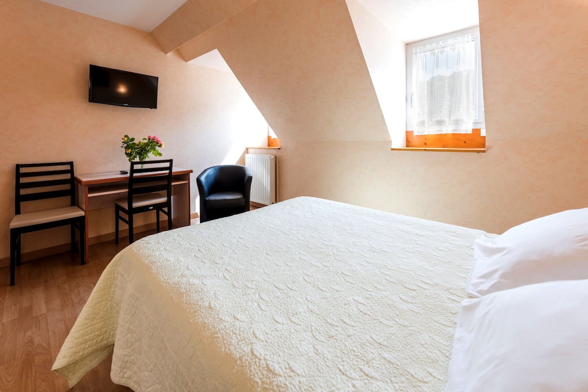 Een slaapkamer met een bed, bureau, stoel en een aan de muur bevestigde televisie.