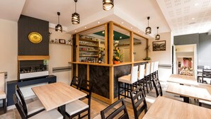 Een restaurant met meerdere tafels en stoelen, een barzone met flessenplanken, en een decoratieve spiegel.