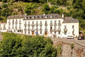 A row of multi-story buildings with balconies, a stone retaining wall, and a street in front. - Hôtel Ardiden (Luz-Saint-Sauveur)