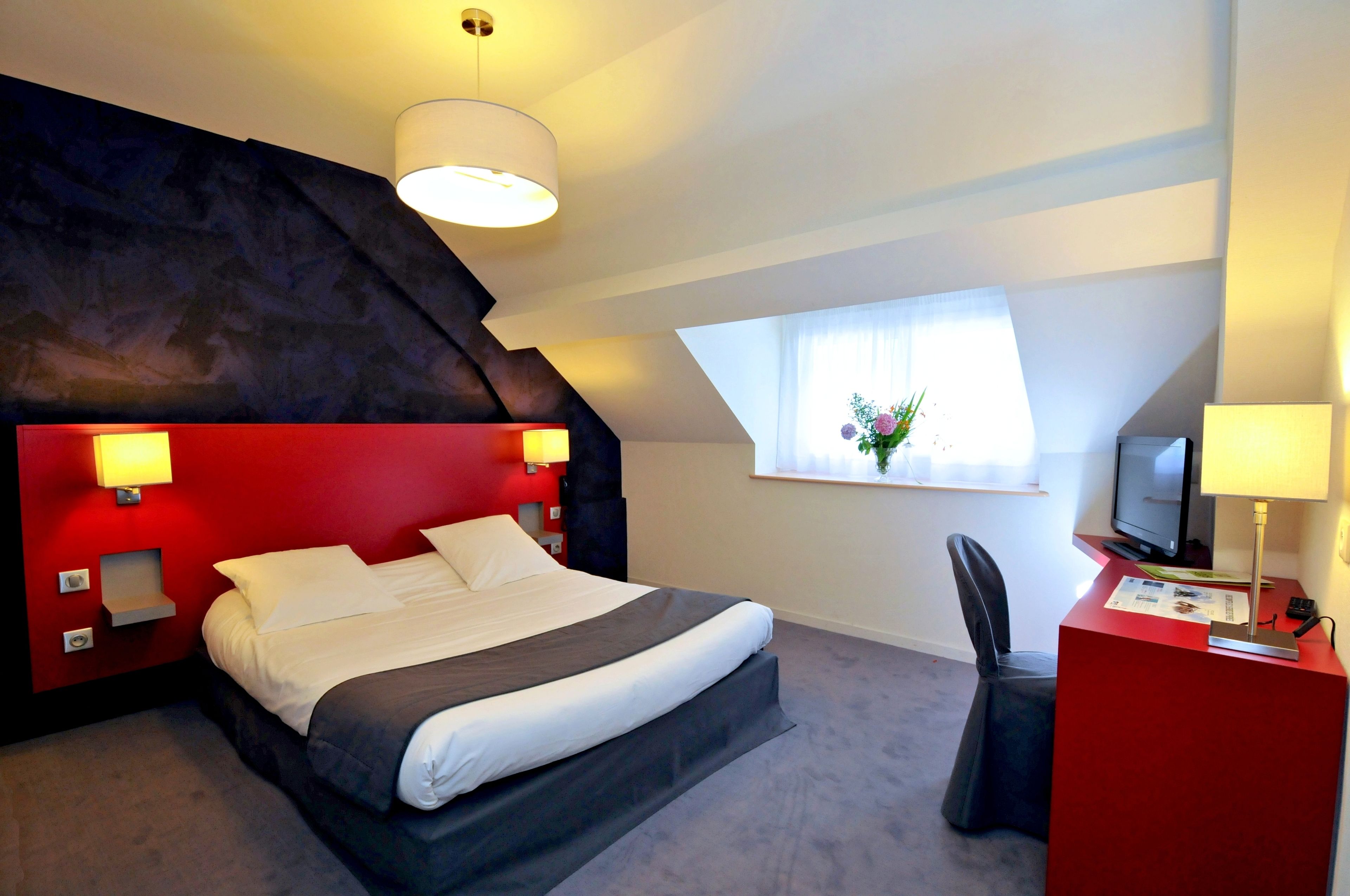 Une chambre d’hôtel moderne, équipée d’un lit, d’un bureau et d’une fenêtre donnant sur un paysage agréable.