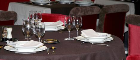 A dining table set with plates, glasses, and cutlery, surrounded by red upholstered chairs.
