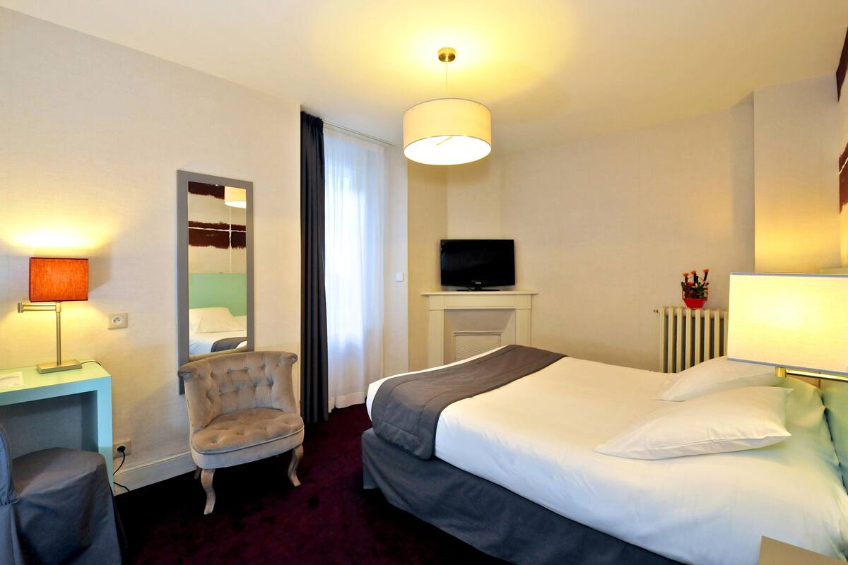 A hotel room with a bed, a chair, a desk, a television, and a mirror.