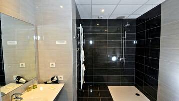 A modern bathroom with a large mirror, a white sink, and a separate shower area with black tiles.