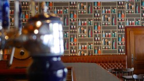 Zona de bar con techo de madera, barra y pared con estanterías que exhiben botellas y copas.