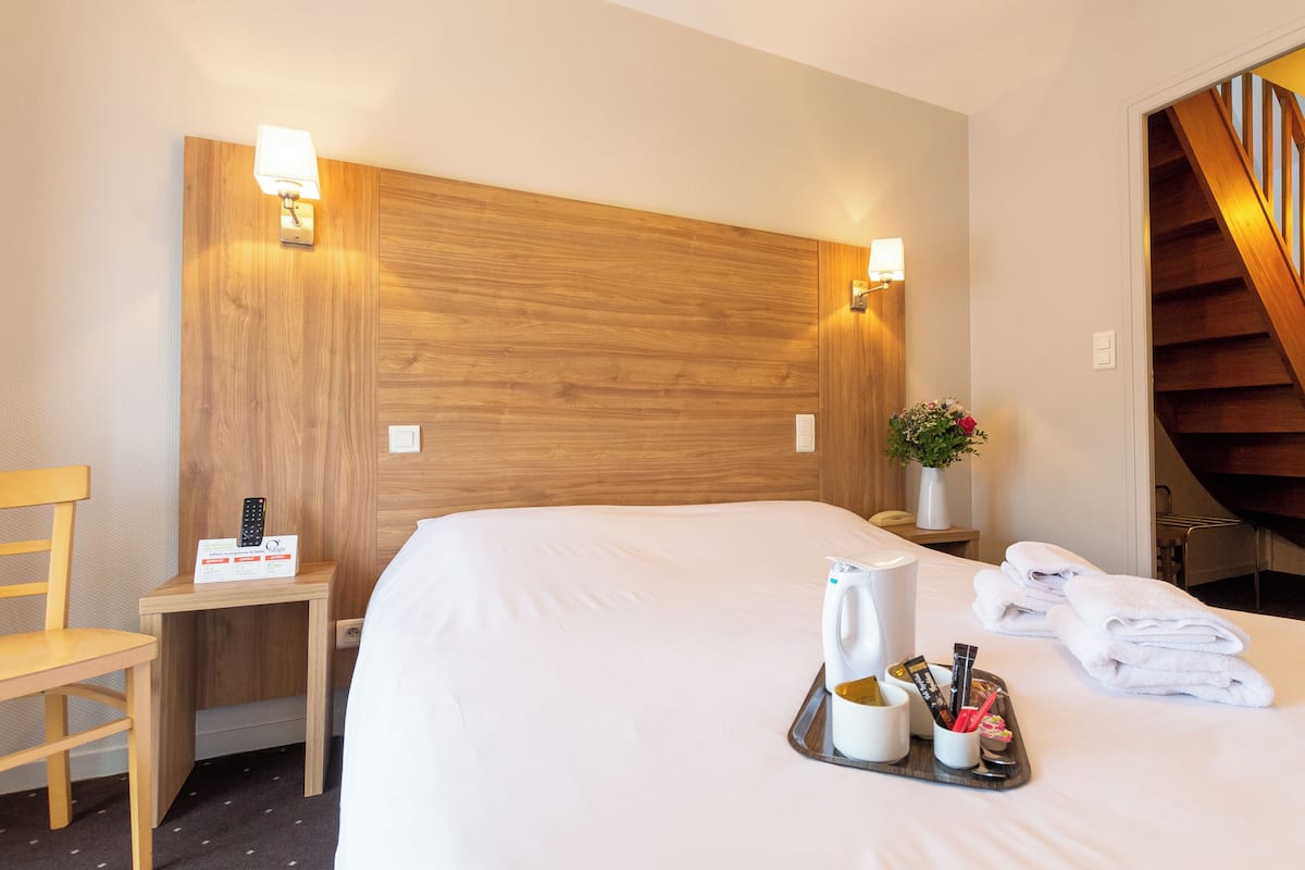 Ein Hotelzimmer mit einem großen Bett, einem Holzkopfstück, Nachttischlampen, einem Holzstuhl, einem kleinen Tisch mit einem Tablett mit Pflegeprodukten und einer Treppe.