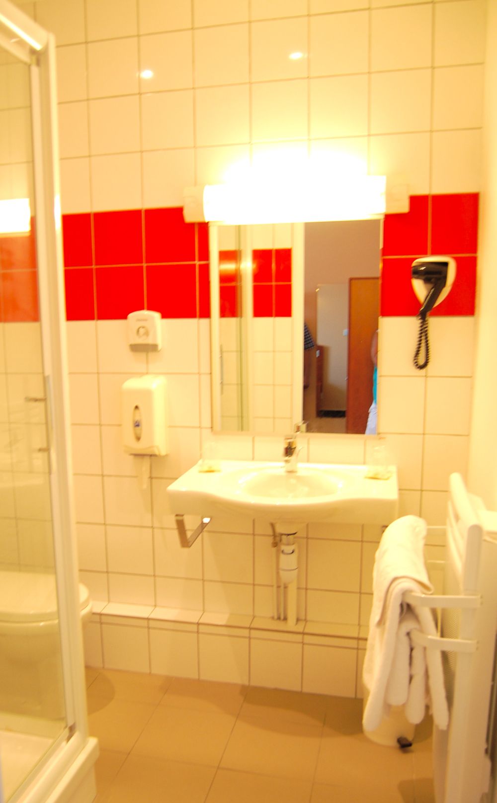Un baño con lavamanos blanco, espejo, secador de pelo y toallero.