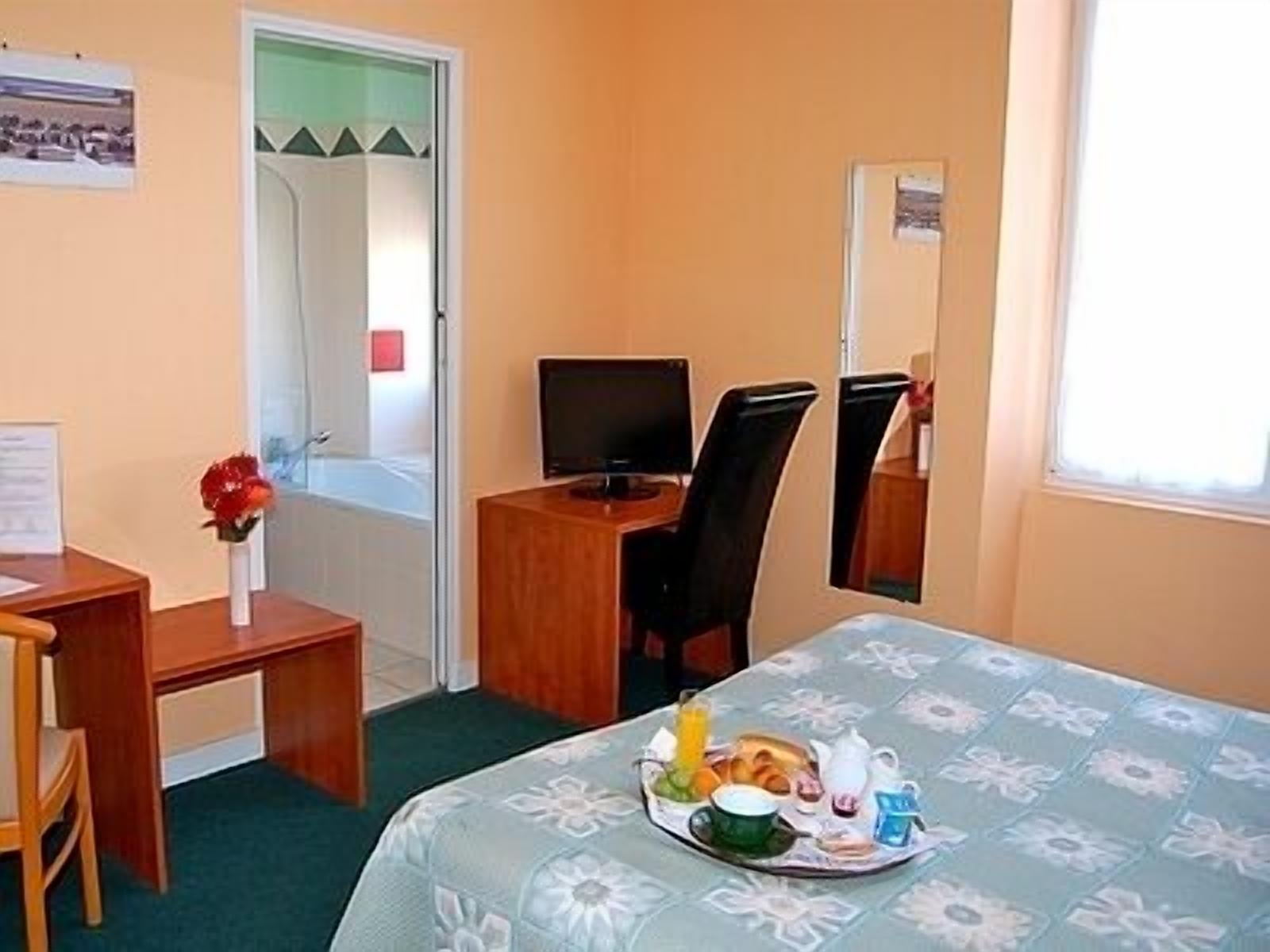 Hotelkamer met een bed, een bureau, een stoel, een televisie en een ontbijt karretje op het bed.