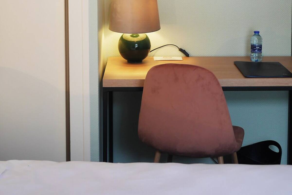 Ein Hotelzimmer mit einem Bett, einem Schreibtisch mit Lampe, einem Stuhl und einer Wasserflasche.