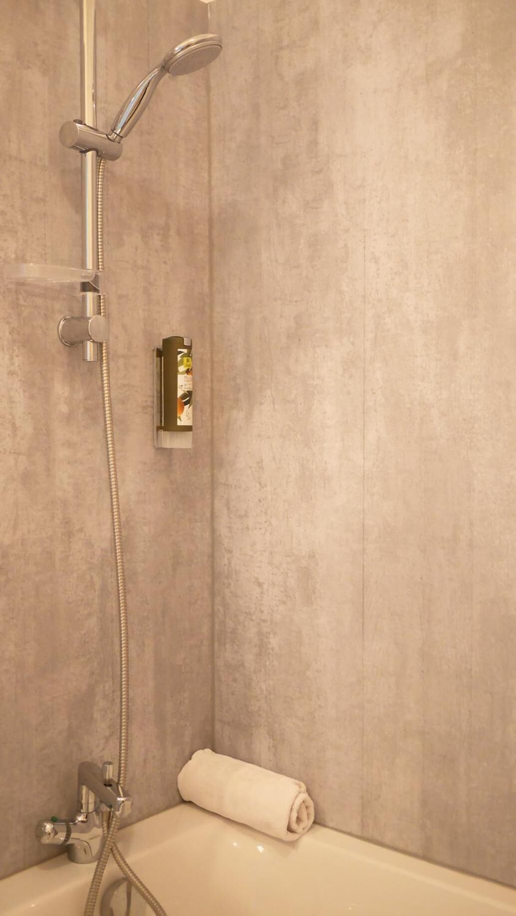 Un baño con bañera, ducha con cabezal de ducha manual y una toalla enrollada en el borde de la bañera.