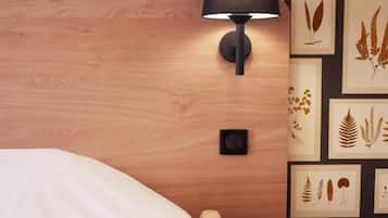A hotel room with a bed, a bedside table, a lamp, and a wall decorated with framed botanical prints.
