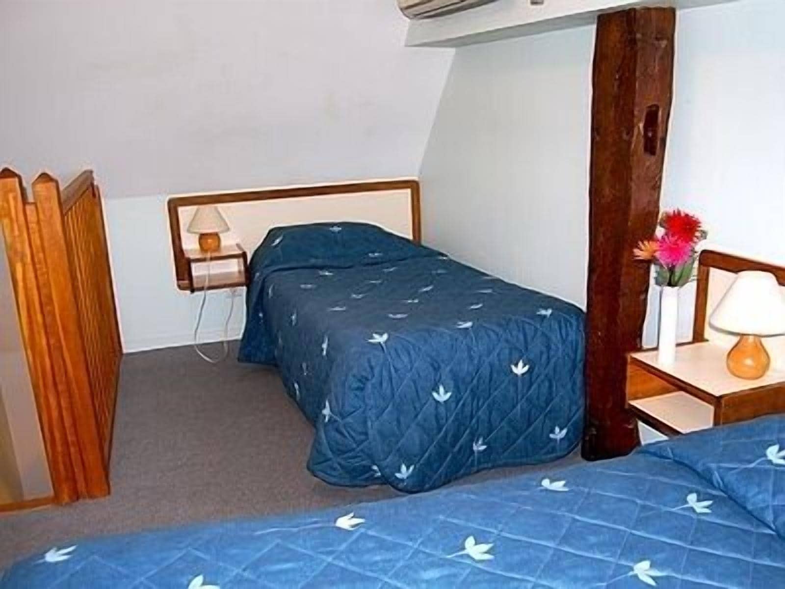 Une chambre avec deux lits, une tête de lit en bois, une table de chevet avec une lampe et un vase rempli de fleurs.