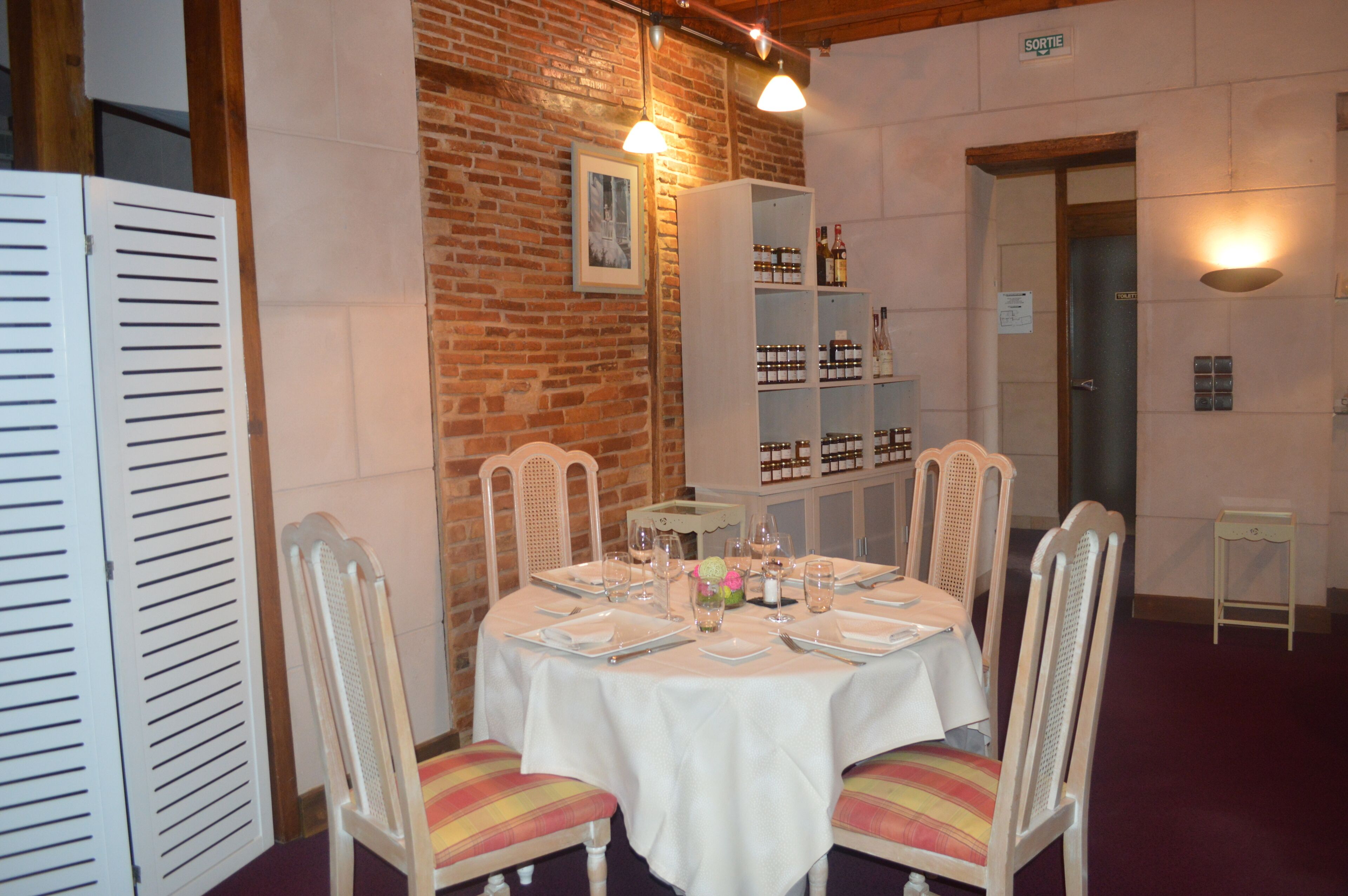 A dining area with a brick wall, white chairs, a round table set for four, and a wine rack in the background.