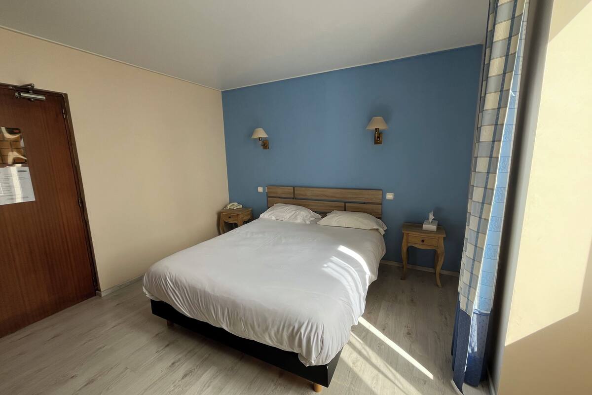 Ein Schlafzimmer mit einem Bett, einem Holz-Kopfstück, Nachttischen, einer Nachttischlampe und einer Tür.