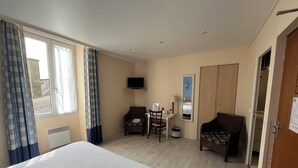 Een hotelkamer met een bed, een bureau met stoel, een televisie, een spiegel en een kledingkast.